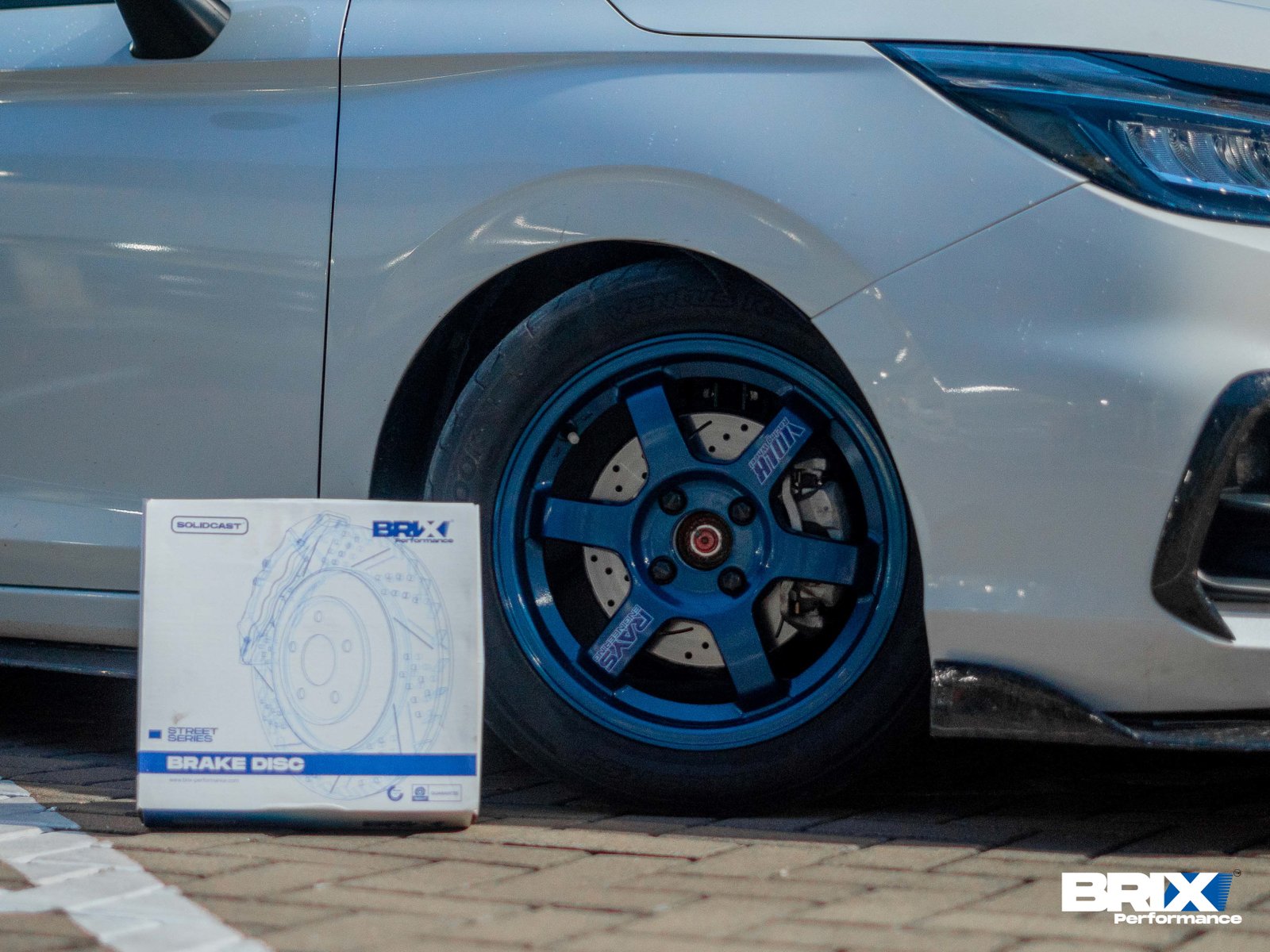 Front wheel and BRIX Performance brake rotor on Honda City Hatchback with blue Volk Racing wheels.